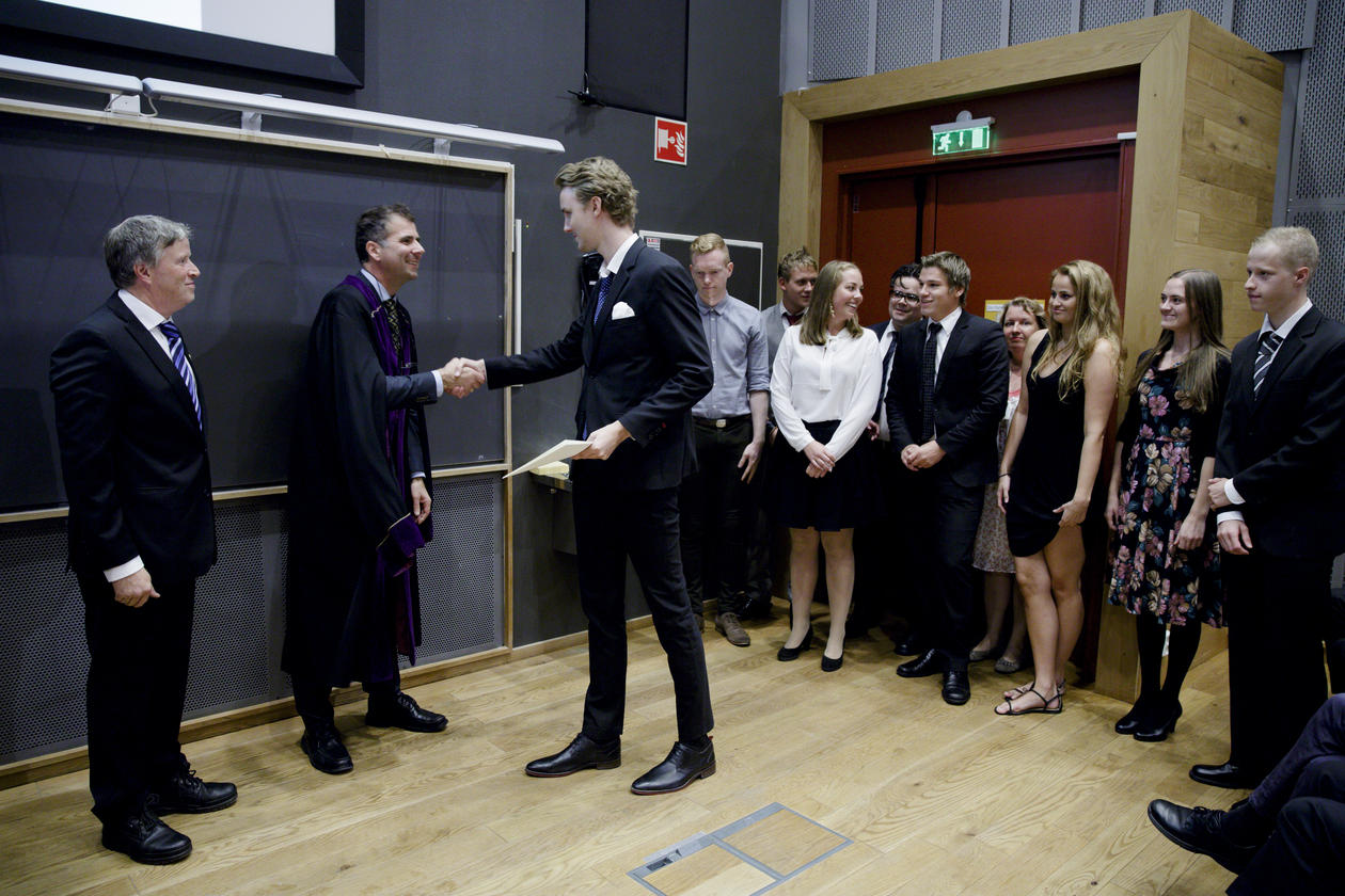 Kandidatene står på podiet og tar imot vitnemålet fra dekan og instituttleder en etter en.