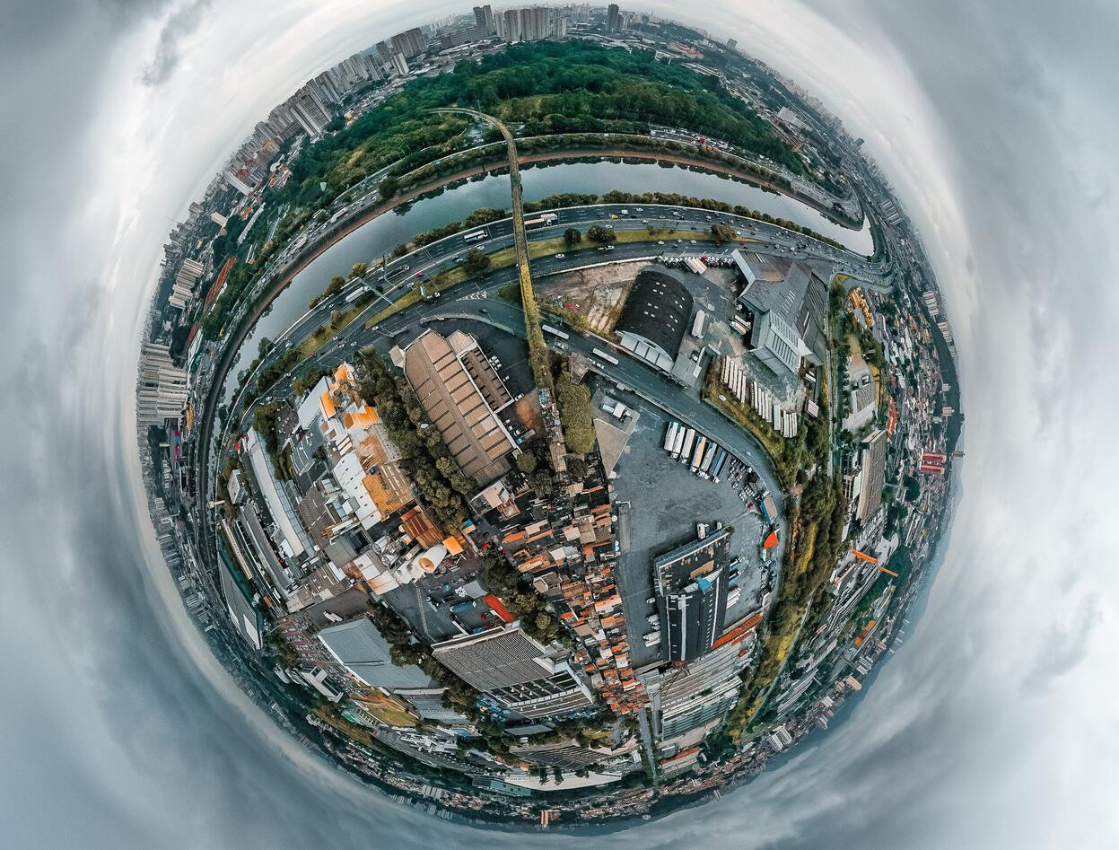 A picture of a city with the stereographic projection effect, making it look like a globe. It has an industrial section and a park with some buildings. The surrounding sky is gray and cloudy