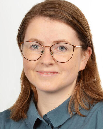 Portrait photo of a young woman with glasses and medium long hair in a blue shirt