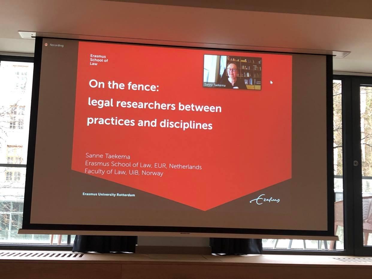 A powerpoint projected on a large screen - red background and the text: On the fence: legal researchers between practices and disciplines