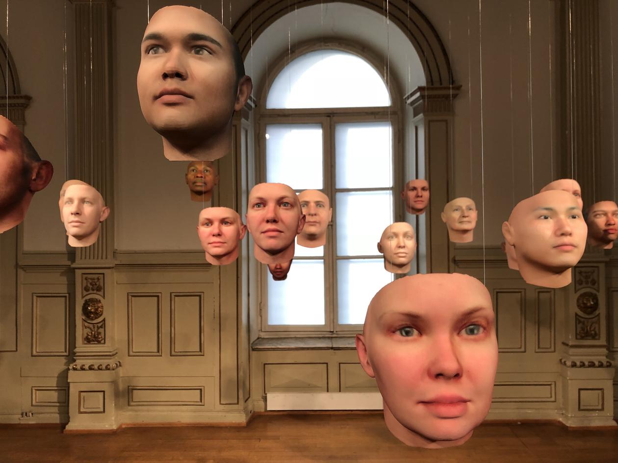 Bilde av datagenererte masker som henger i luften i et galleri.