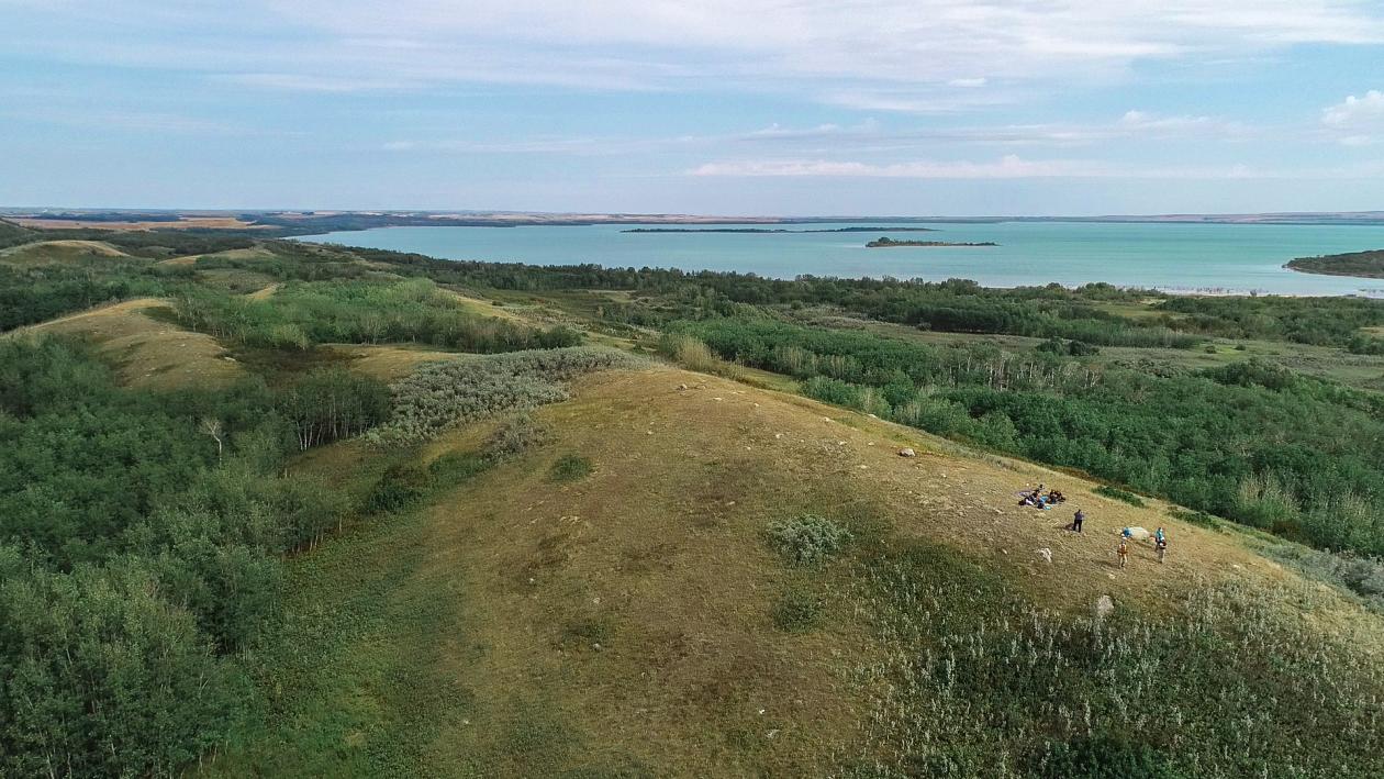 A landscape view of partly wooded, partly open slightly hilly terrain looking across to a large lake with two small islands