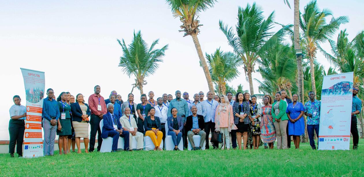 People standing outside on a green lawn for a group photo. Palm trees in the background.