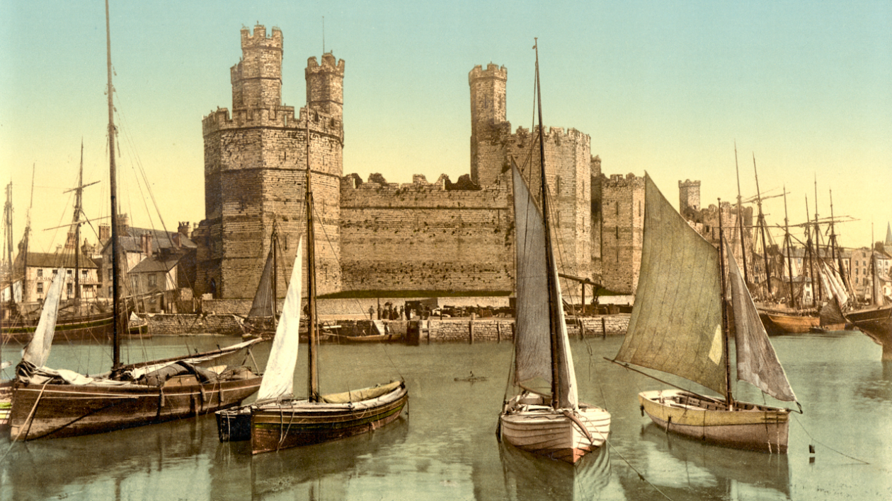 Fargefoto av plass i Wales i 1890-åra. Nokre båtar på vatn framfor ei borg frå mellomalderen.