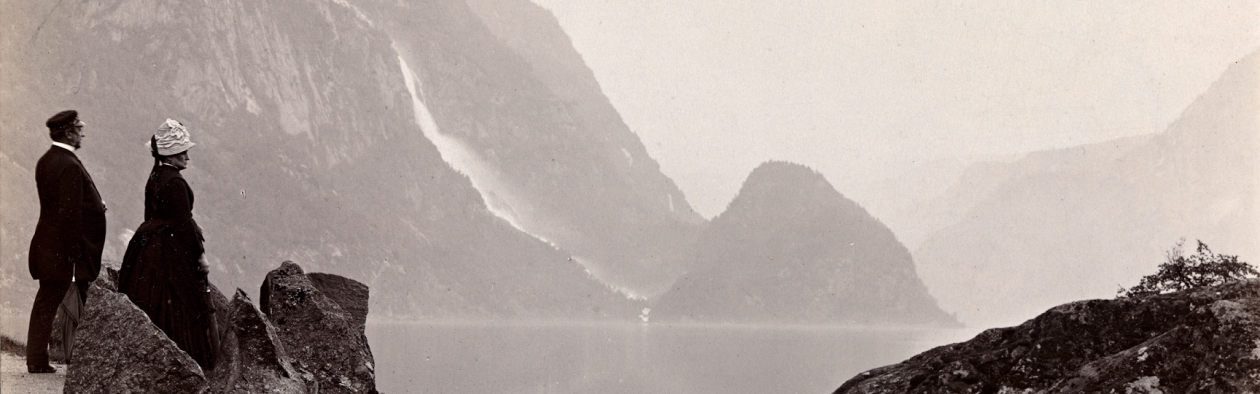 Hardanger i 1882. Ein middelaldrande mann og ei dame, sannsynlegvis eit par, stirrar på fjord og fjell. Ein foss skimtast i bakgrunnen