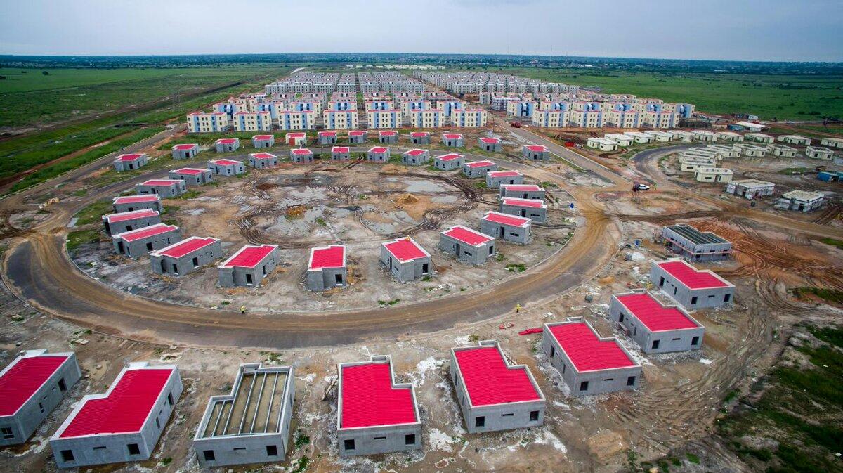 drone photo of an abandon buliding site, showing several houses built in a circle formation. Those that have a roof has a bright red roof. 