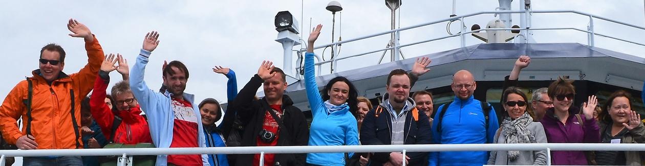 A group of people waving from the top deck of a ship. 