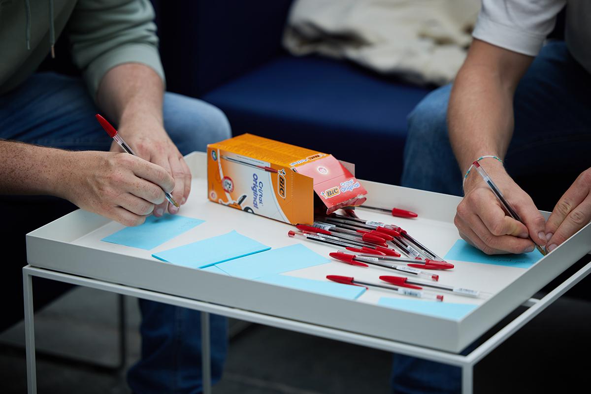The picture shows hands from two people writing on post-it notes.