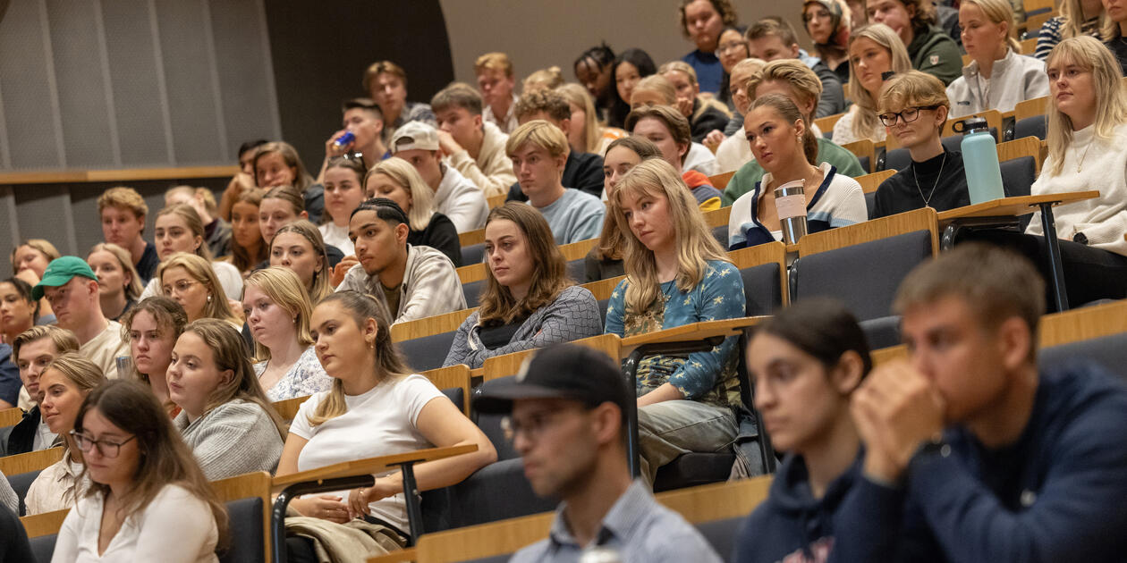 Bildet viser mange studenter sittende i en forelesningssal.
