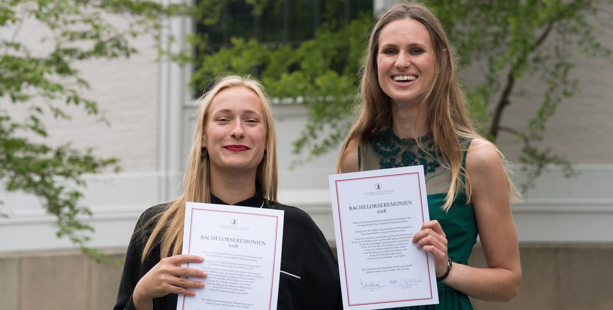 To blide studenter i muséhagen med sine diplomer
