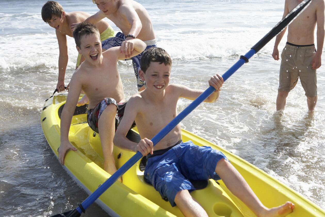 Tenåringsgutter leker i vannkanten med en gul kajakk 