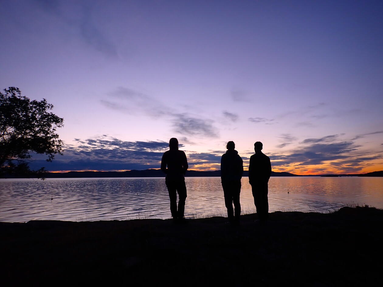 Silhouettes of three persons by the water at sunset