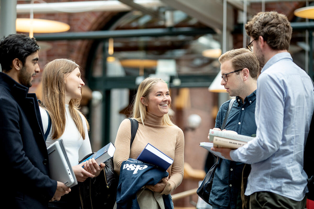 Bildet viser en gruppe studenter som står i en gruppe og snakker sammen i foajeen på Dragegjellet, Jussbygget ved UiB.