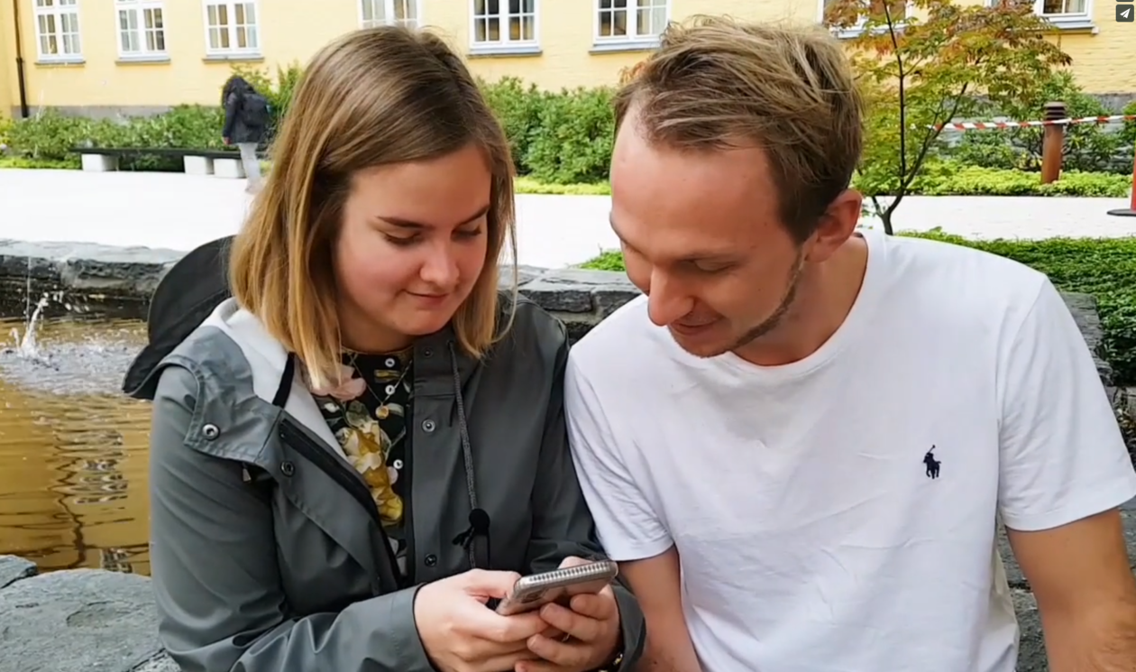 Jente og gutt sitter foran Sydneshaugen skole og ser sammen på mobiltelefon for å teste hubro chatbot
