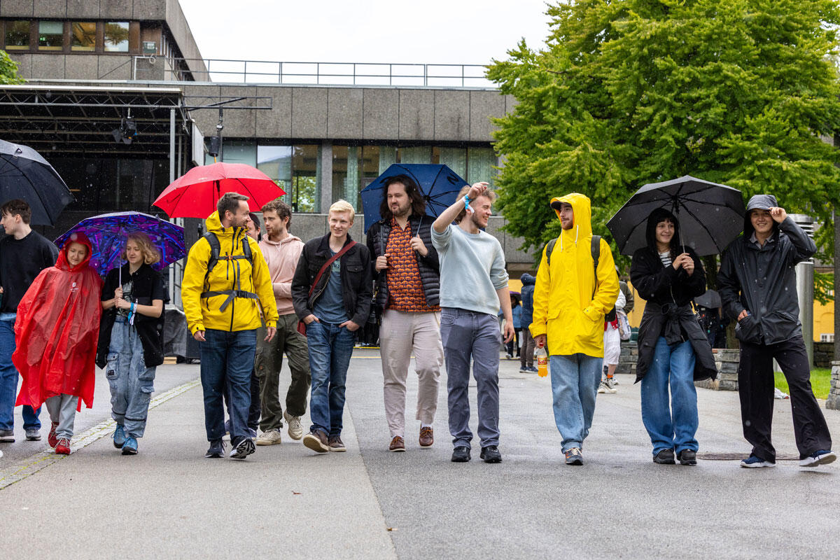 En gruppe studenter går ute i regnvær med regntøy og paraplyer