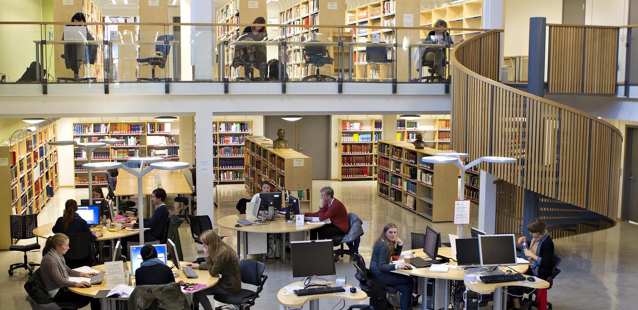 Bilde fra bibliotek for humaniora der flere studenter sitter rundt bord og arbeidsstasjoner og jobber.