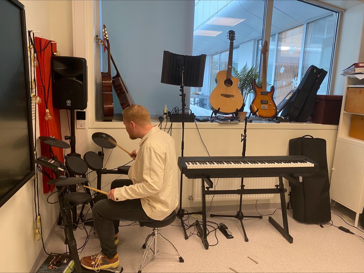 mann spiller trommer på et musikkrom med mange musikkinstrumenter