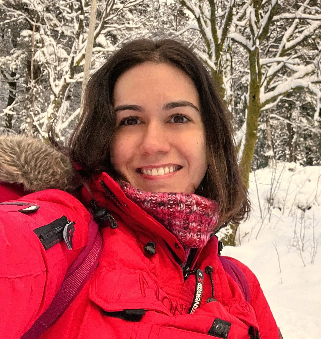 Portrettfoto av Maria Miguez i rød anorakk med snødekt skog i bakgrunnen