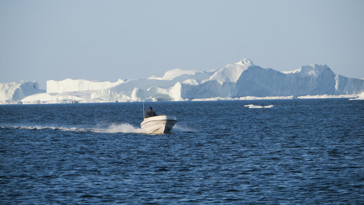 Grønlender i full fart med motorbåten sin fremfor isfjell.