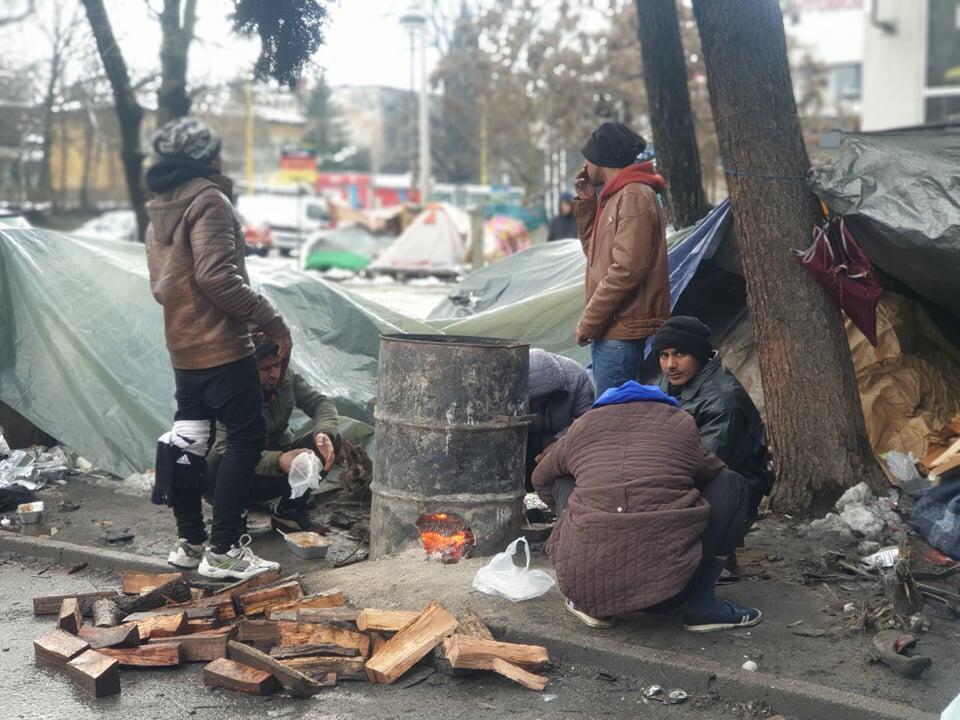 Migranter samler seg rundt et bål ved Tuzia busstasjon