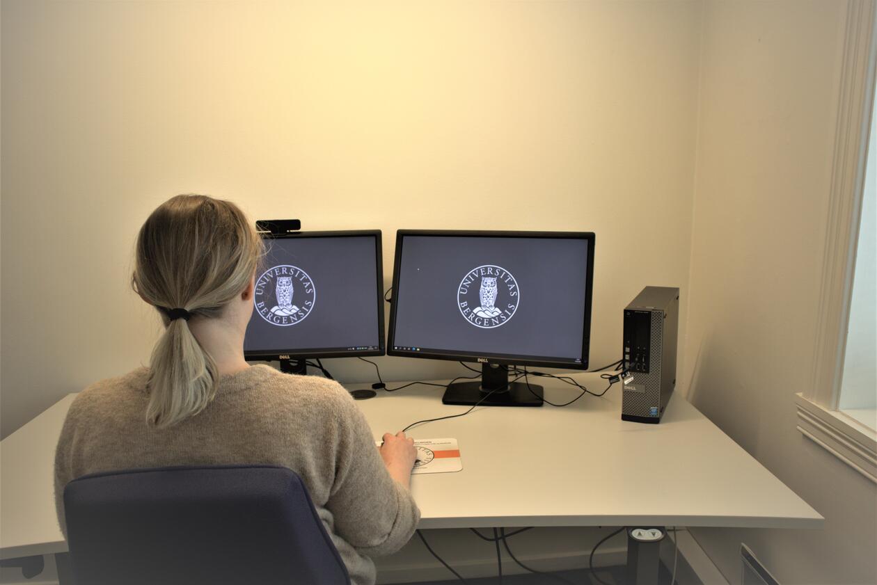 Kvinne som sitter foran to skjermer. Hovedskjerm er plassert rett fremfor kroppen, sekundærskjerm er plassert ved siden av denne.