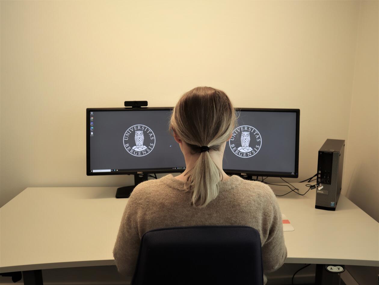 Kvinne som sitter foran to skjermer. Midtlinjen mellom skjermene går rett foran kroppen.