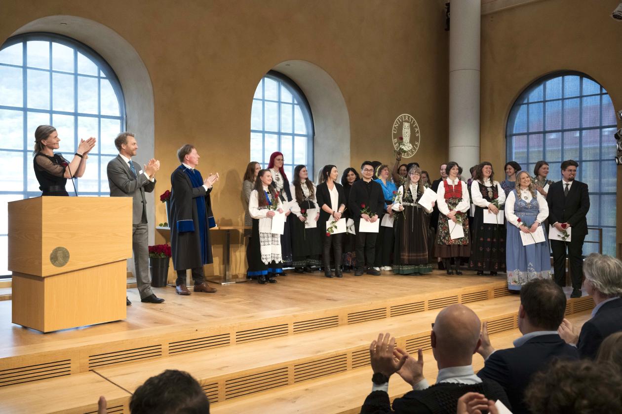 Masterstudenter samlet på scenen i aulaen.