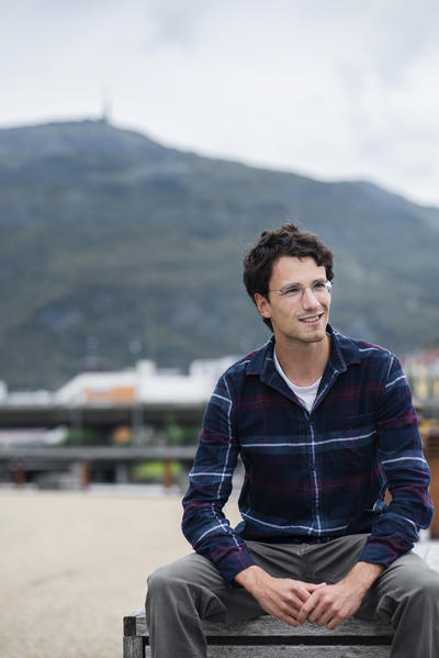 A male student sitting on a bench with Mount Ulriken in the distant background