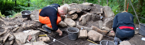 Arkeologar sit i ein steinhaug rekonstrurer ei grav