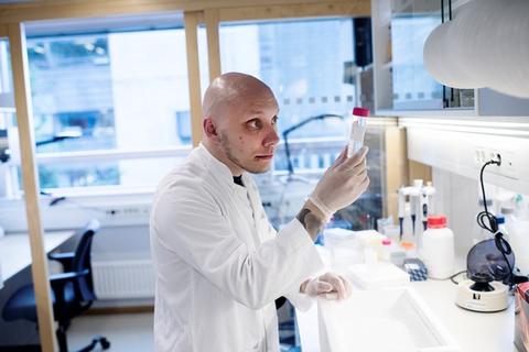 A student in a lab coat working in a lab, holding up a test tube.