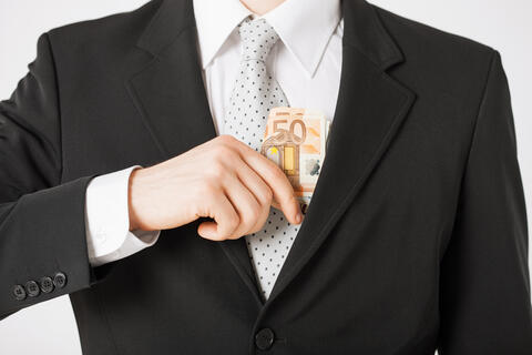 Illustration photo of man in suit and tie putting money in his inner breast pocket. Used to illustrate article on corruption.