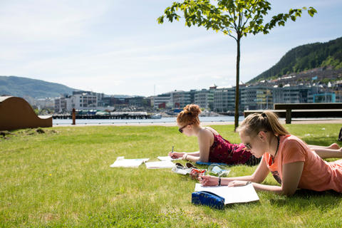 Two female students reading on the lawn outside with ocean view. 