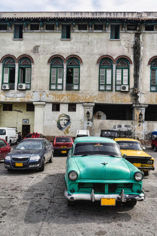 Picture of an old car in Havana with street art of Che Guevara on a building in the background