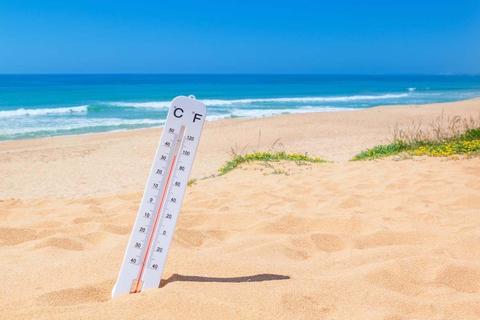 Thermometer stuck in the sand on a beach, showing scorching heat, image used to accompany an article on heat waves and climate change.