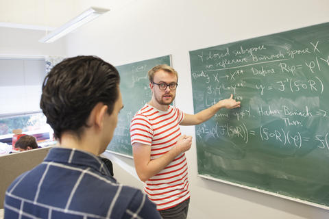 En student viser en annen student matematiske formler på en tavle