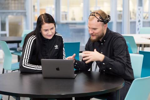 IT-utdanning: Bildet viser to studenter som sitter ved et bord og ser på en laptop og prater.