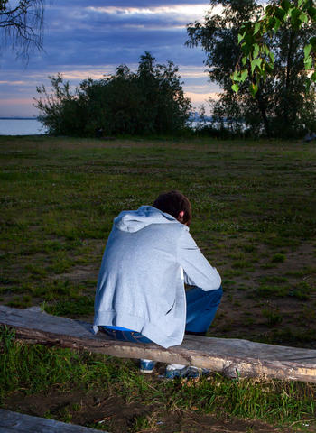 Trist ung mann som sitter med ryggen til på en benk i en park i skumringen 