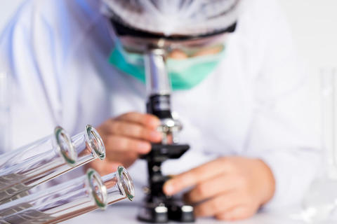 Blurry picture of researcher looking into a microscope, photo used to illustrate article about candidates for the Centre of Excellence scheme.