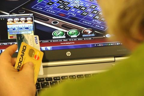 En person med flere kredittkort i hånden sitter foran dataskjermen og ser på et pengespill.