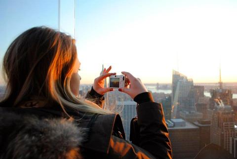 En jente ser ned på en storby fra et høyt tårn og tar bilde av solnedgangen