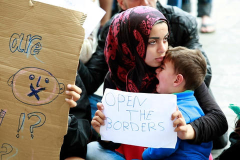 Kvinne med barn på flukt. Hun holder et skilt der det står "Open the borders"