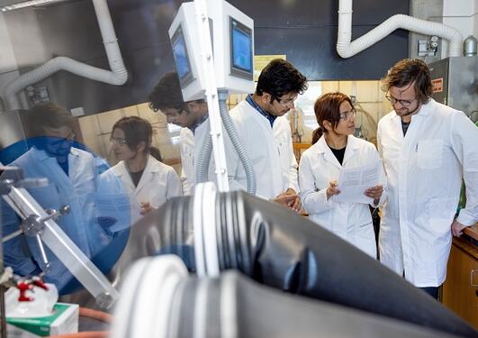 Three scientists discussing a paper or report, pictured with a large glove box in front