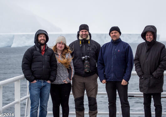 A group of people standing on deck of a vessel, with arctic background