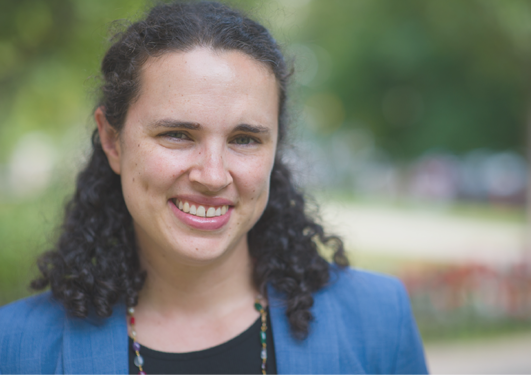 A woman with dark, curly hair, black top and a blue jacket