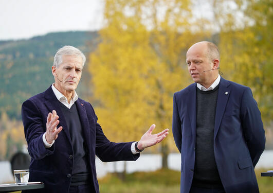 To menn i mørke klær, en åsside og et tre med gule blader i bakgrunnen