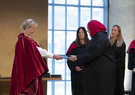 Bilde av ny doktor som får diplom av rektor på scenen i Universitetsaulaen 