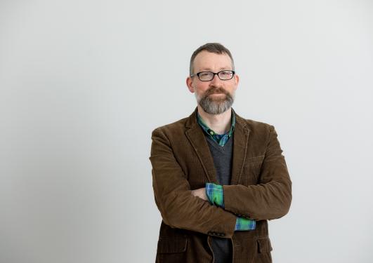 Bildet viser forskeren. En mann med briller og brun blazer. 