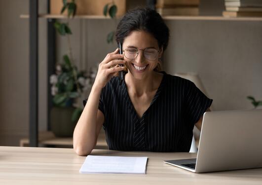 Smiling woman on a phone call. Sitting by a desk with her computer. 