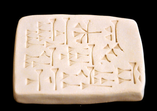 Antikk kileformet tavle med assyriske tegn mot svart bakgrunn