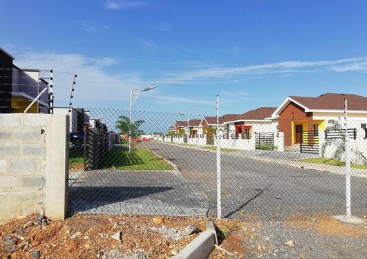 Image taken from outside a security fence, showing a road of neat and orderly suburban houses.  